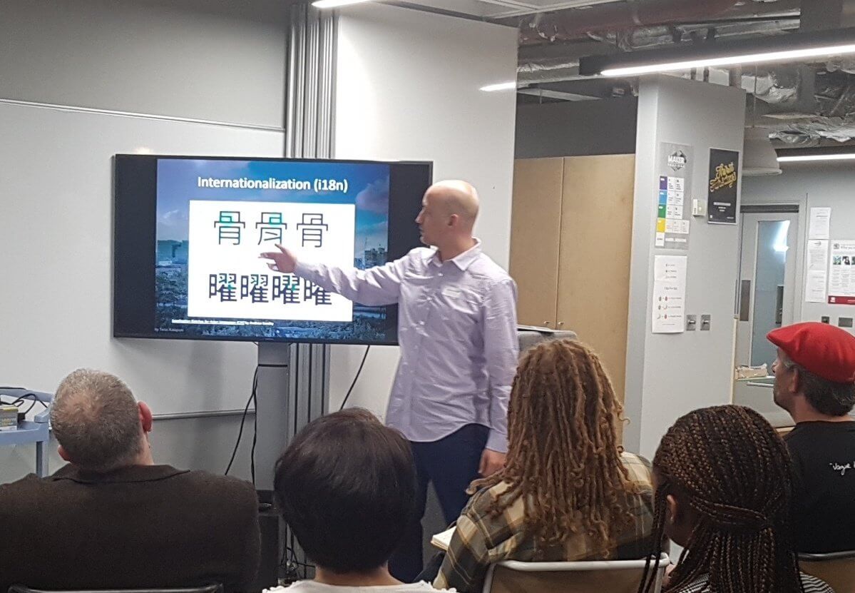 Adrian pointing at a slide showing subtle rendering differences of the same Chinese character, depending on which language it is being rendered for.